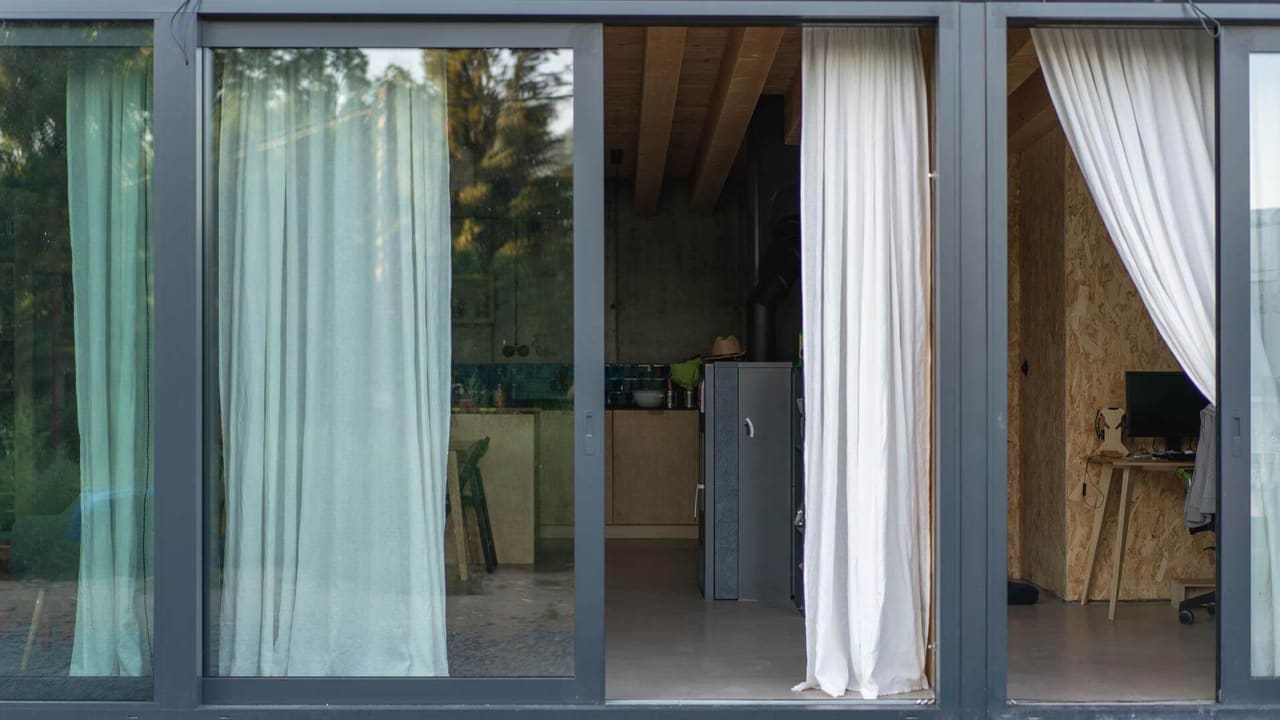 Sliding glass doors of an earth-sheltered house reveal a kitchen and home office with OSB walls and wood beams