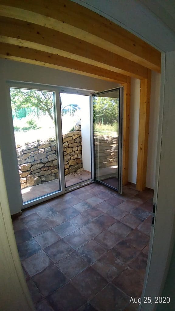 Earth-sheltered home interior with terracotta floor and curved beams opening to a stone terrace