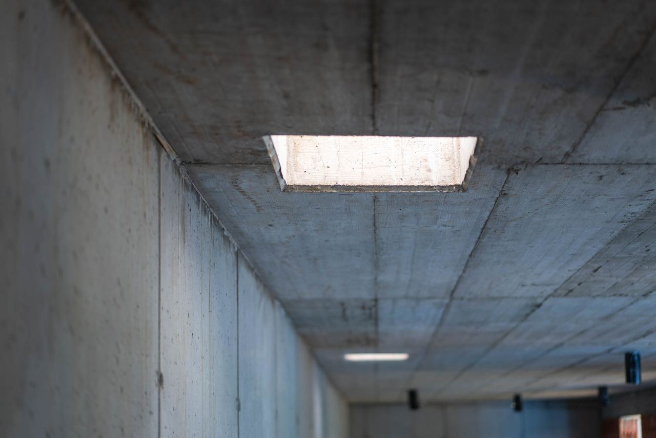 Raw concrete corridor ceiling with board-formed texture and skylight opening in earth-sheltered house